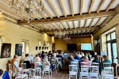 Château éclairé de nuit avec des lumières colorées, entouré de buissons et de tentes blanches sous un ciel nuageux.