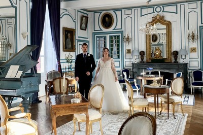 Château éclairé de nuit avec des lumières colorées, entouré de buissons et de tentes blanches sous un ciel nuageux.