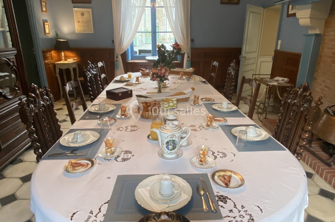 Table dressée pour un petit-déjeuner avec vaisselle, nappe blanche, viennoiseries et décor intérieur chaleureux.