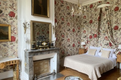 Château éclairé de nuit avec des lumières colorées, entouré de buissons et de tentes blanches sous un ciel nuageux.