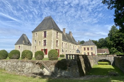 Château éclairé de nuit avec des lumières colorées, entouré de buissons et de tentes blanches sous un ciel nuageux.