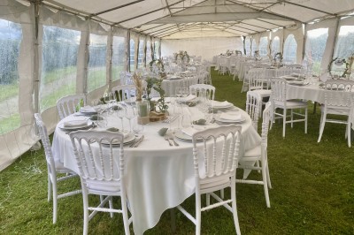 Château éclairé de nuit avec des lumières colorées, entouré de buissons et de tentes blanches sous un ciel nuageux.