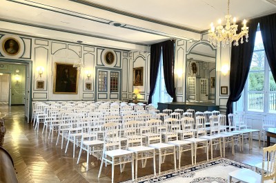Château éclairé de nuit avec des lumières colorées, entouré de buissons et de tentes blanches sous un ciel nuageux.