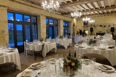 Château éclairé de nuit avec des lumières colorées, entouré de buissons et de tentes blanches sous un ciel nuageux.