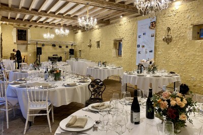 Château éclairé de nuit avec des lumières colorées, entouré de buissons et de tentes blanches sous un ciel nuageux.