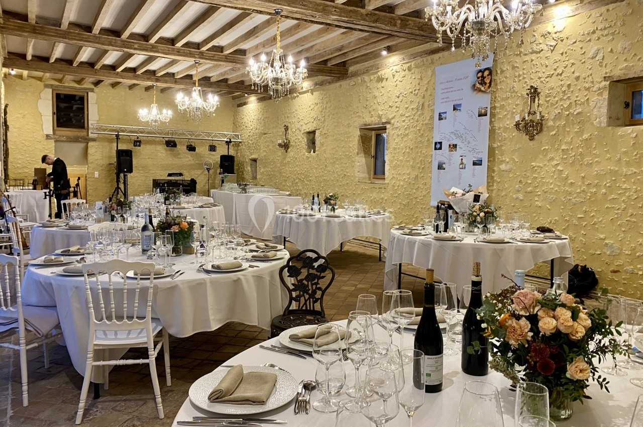 Salle de réception décorée avec des tables rondes dressées, des chandeliers suspendus et des murs en pierre apparente.