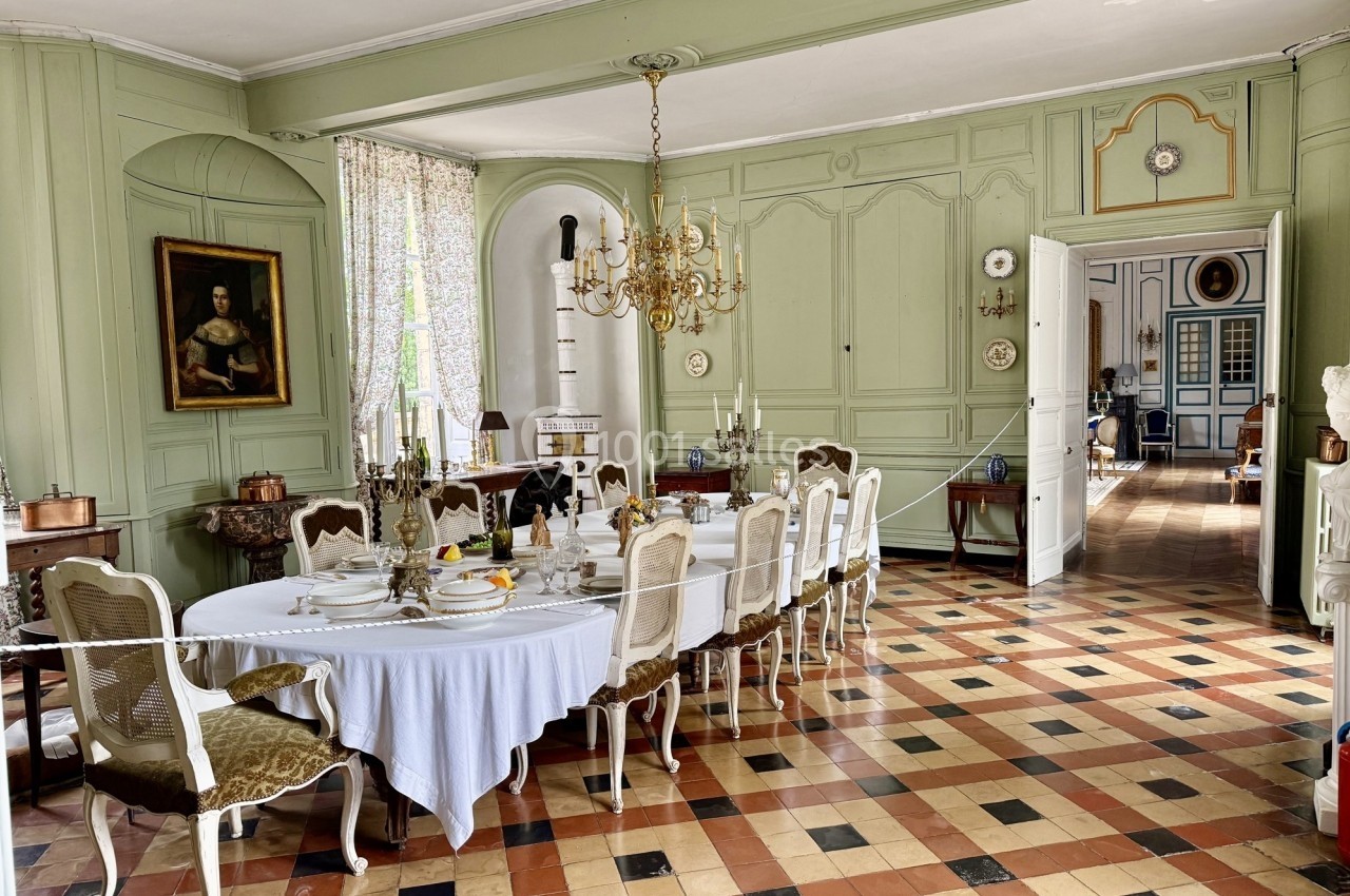 Salle à manger élégante avec table dressée, chaises classiques, lustre doré et murs ornés de boiseries vert pâle.