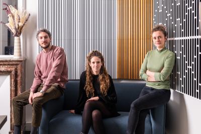 Trois personnes assises et debout dans un intérieur moderne avec des panneaux muraux décoratifs en arrière-plan.