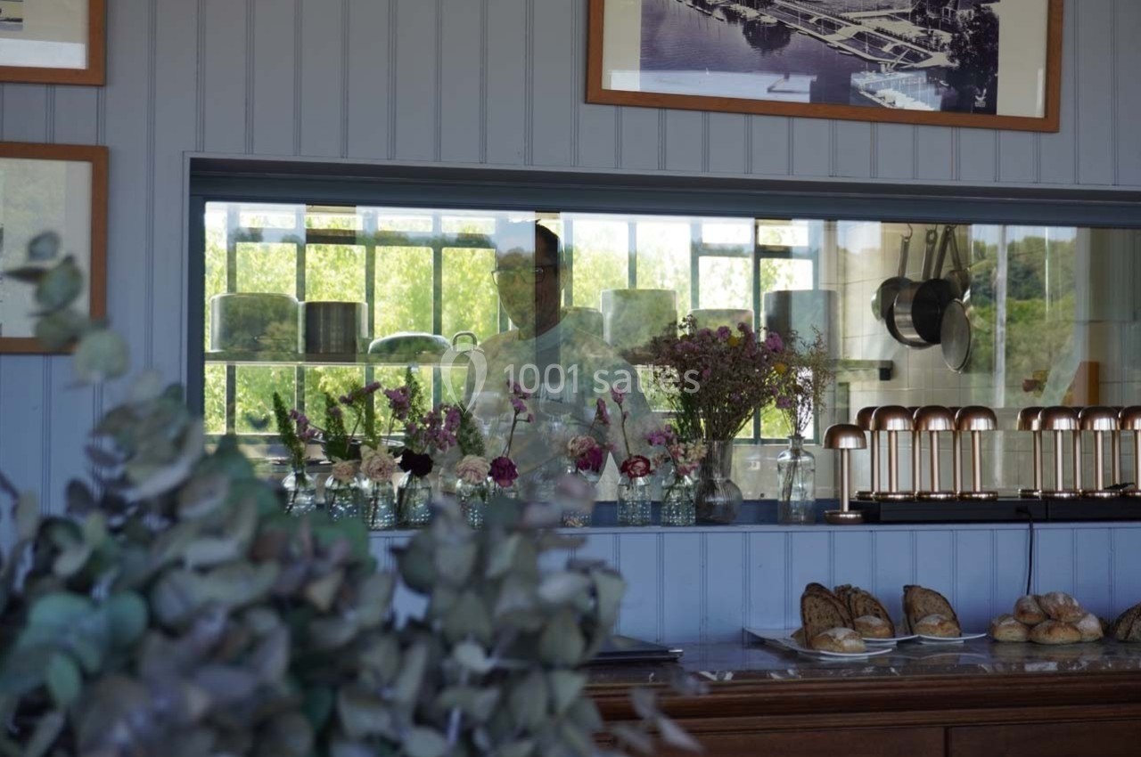 Un comptoir avec des fleurs en vase, des pâtisseries et un cuisinier visible à travers une fenêtre intérieure.