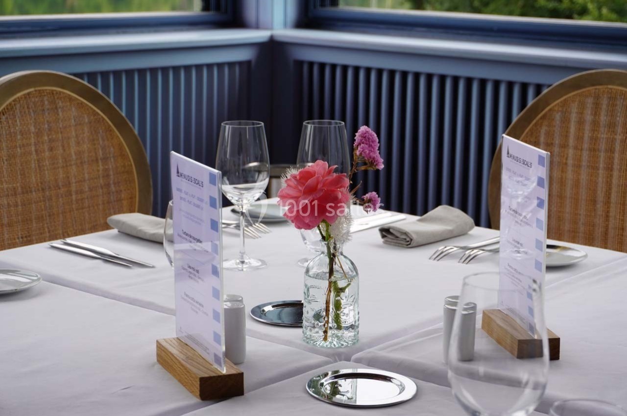 Table dressée avec nappes blanches, menus, verres à vin et vase contenant des fleurs roses et violettes.