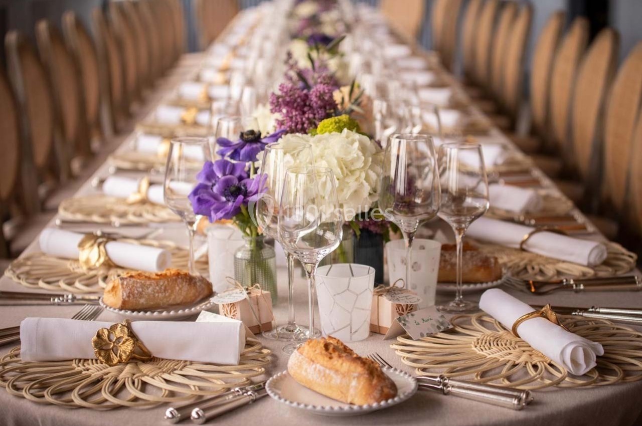 Table élégamment dressée avec des fleurs, des verres à vin, des assiettes et des serviettes ornées de décorations dorées.