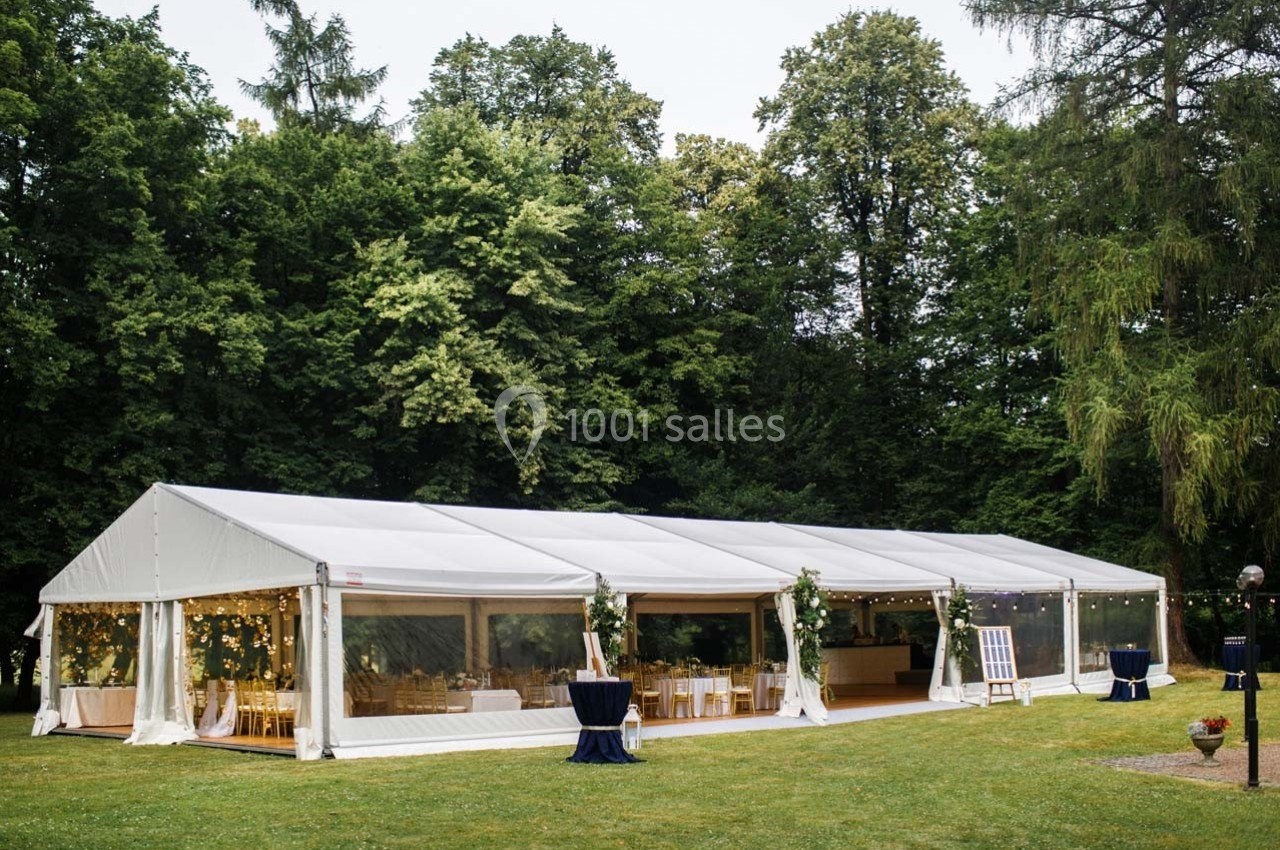 Tente blanche installée dans un jardin verdoyant, décorée de guirlandes lumineuses et aménagée pour un événement.