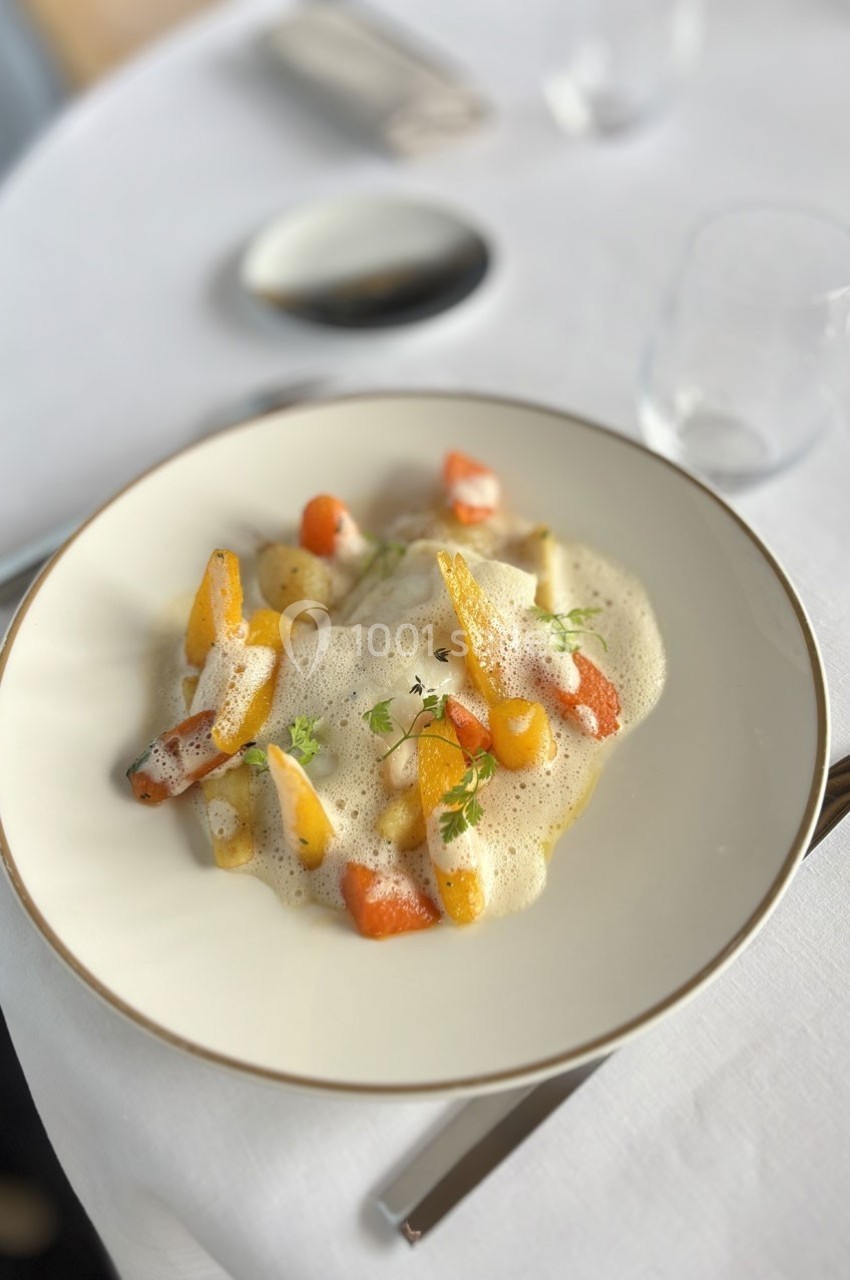 Assiette de légumes colorés nappés d'une mousse légère, présentée sur une table dressée avec élégance.