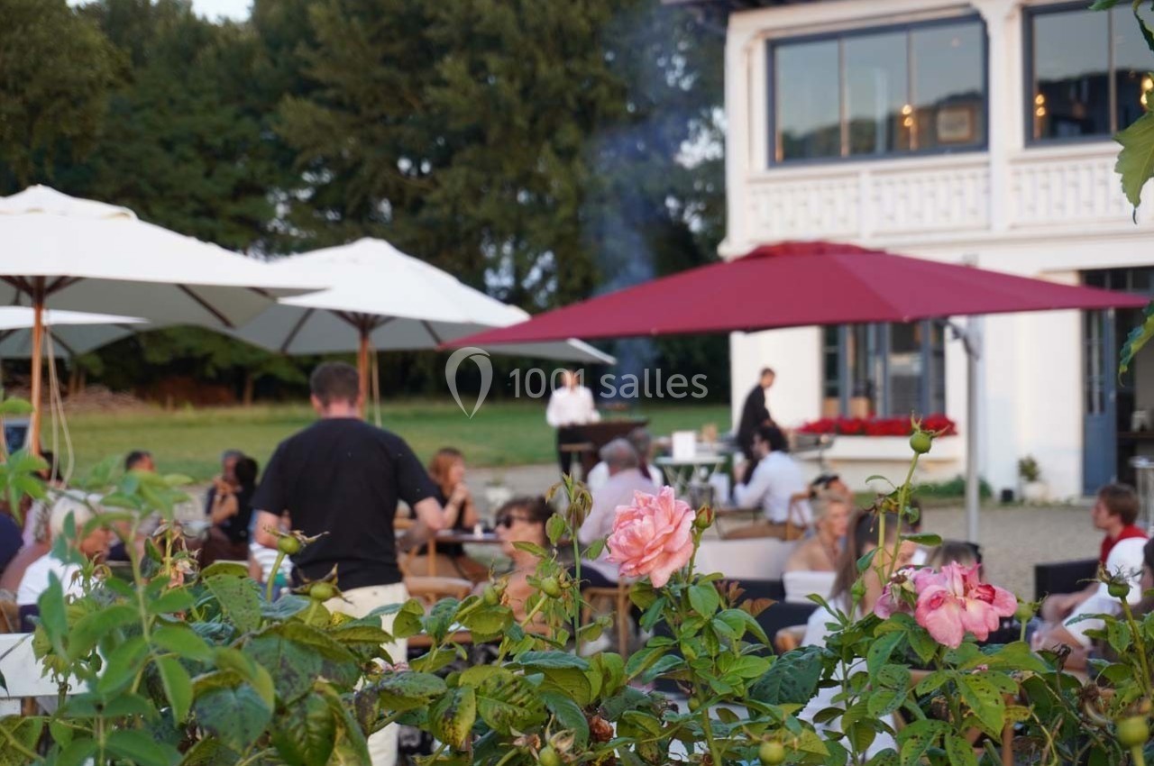 Terrasse animée d'un restaurant avec des clients attablés, des parasols et des fleurs au premier plan.