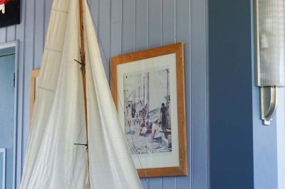 Maquette de voilier avec une grande voile blanche exposée devant un mur bleu orné de cadres et d'une applique murale.
