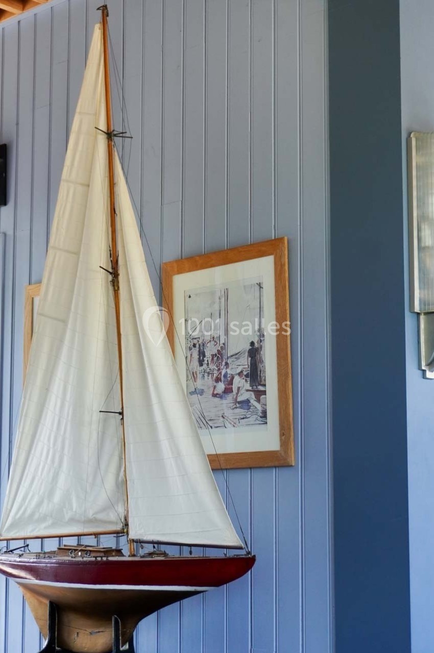 Maquette de voilier avec une grande voile blanche exposée devant un mur bleu orné de cadres et d'une applique murale.