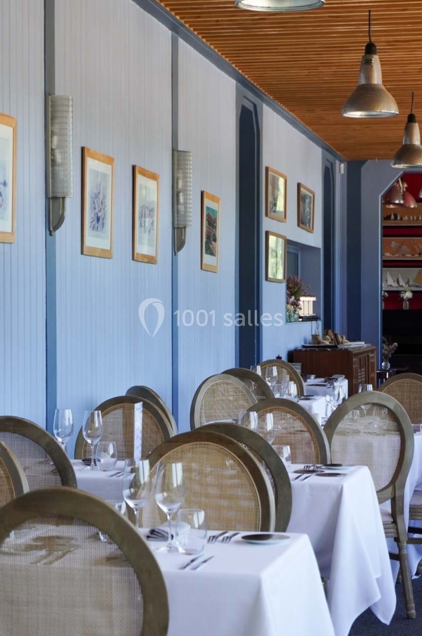 Salle de restaurant élégante avec tables dressées, chaises en osier et décorations murales encadrées.