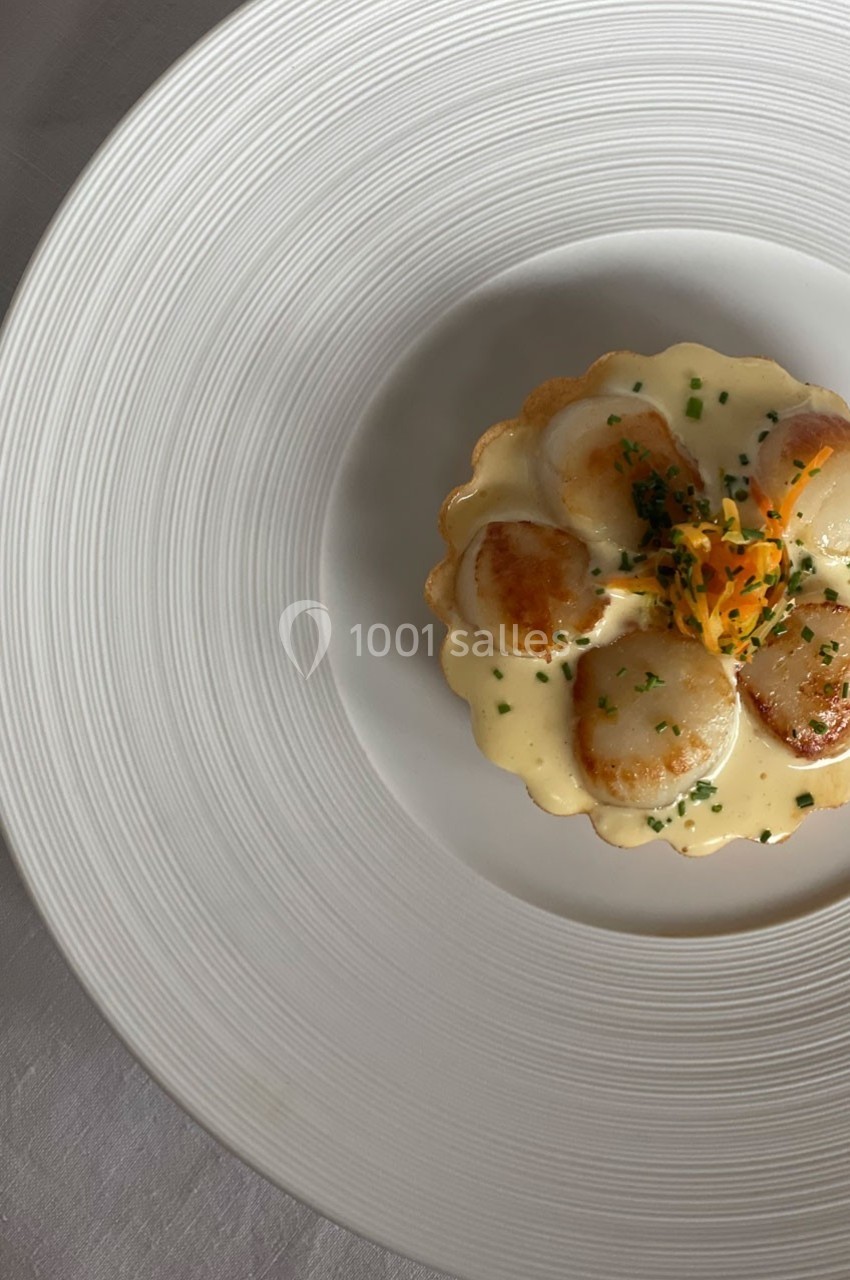 Tartelette garnie de noix de Saint-Jacques poêlées, nappée de sauce crémeuse et décorée de fleurs comestibles.