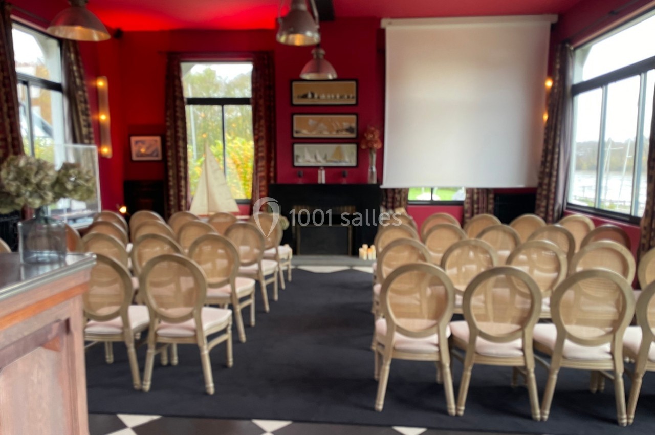 Salle de réunion avec chaises alignées face à un écran de projection, éclairée par des fenêtres et des lumières suspendues.