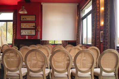 Salle de réunion avec une table en bois, des chaises en osier, des bouteilles d'eau et des documents, vue sur l'extérieur.