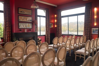 Salle de réunion avec une table en bois, des chaises en osier, des bouteilles d'eau et des documents, vue sur l'extérieur.