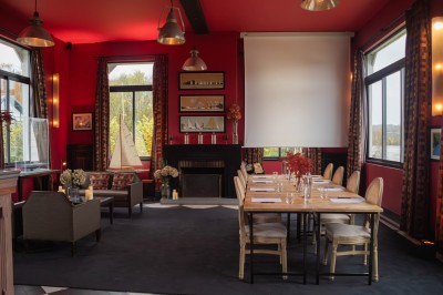 Salle de réunion avec une table en bois, des chaises en osier, des bouteilles d'eau et des documents, vue sur l'extérieur.