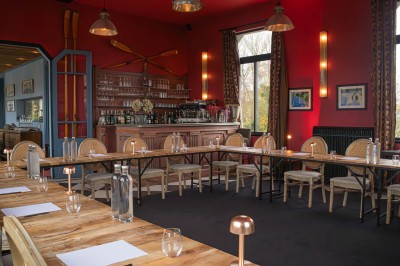 Salle de réunion avec une table en bois, des chaises en osier, des bouteilles d'eau et des documents, vue sur l'extérieur.