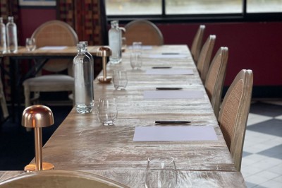 Salle de réunion avec une table en bois, des chaises en osier, des bouteilles d'eau et des documents, vue sur l'extérieur.