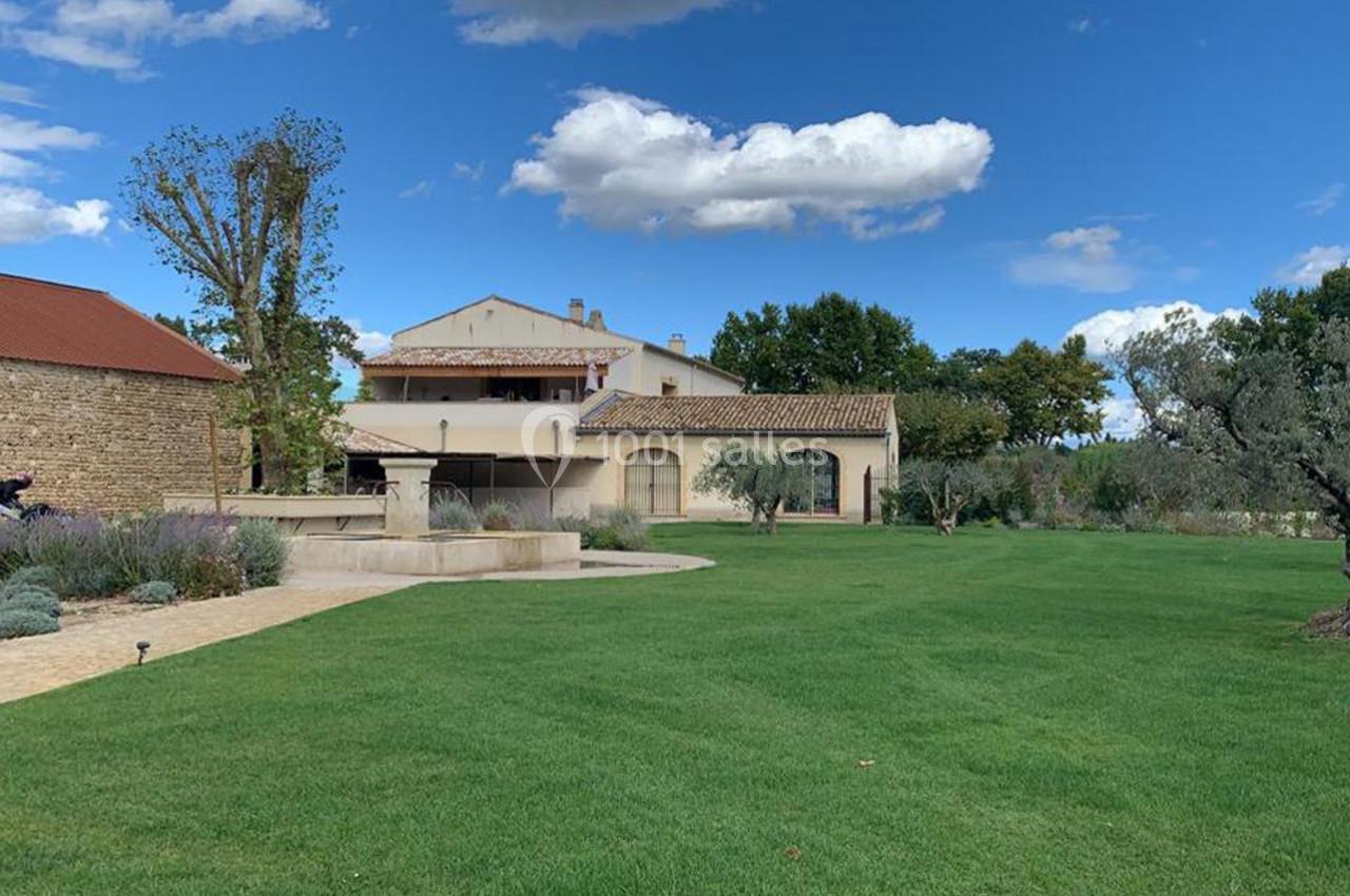 Grande maison provençale entourée de pelouse, d'arbres et d'un ciel bleu avec quelques nuages.