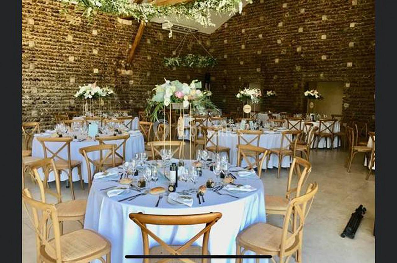 Salle de réception décorée avec des tables rondes dressées, nappes blanches, chaises en bois et compositions florales.