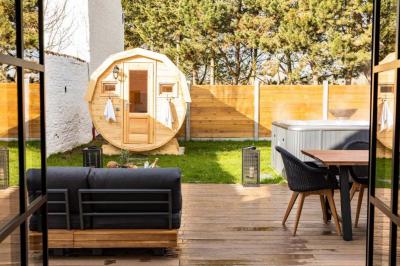 Terrasse en bois avec salon de jardin, sauna en forme de tonneau, jacuzzi et clôture en bois, entourée de verdure.