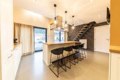 Terrasse en bois avec salon de jardin, sauna en forme de tonneau, jacuzzi et clôture en bois, entourée de verdure.