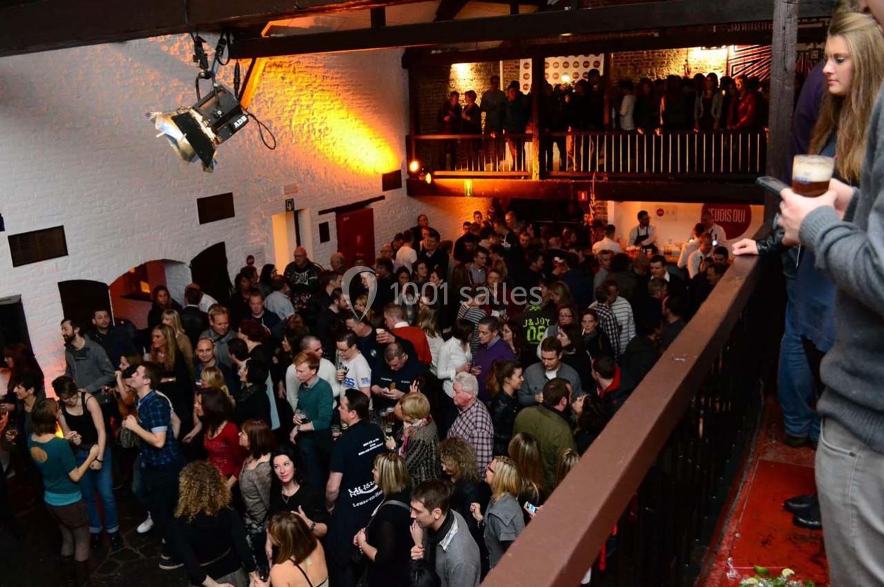 Foule rassemblée dans une salle avec mezzanine, éclairée par des lumières chaudes, ambiance festive.