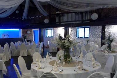 Salle de réception décorée avec des tables rondes, nappes blanches, chaises houssées et éclairage tamisé.