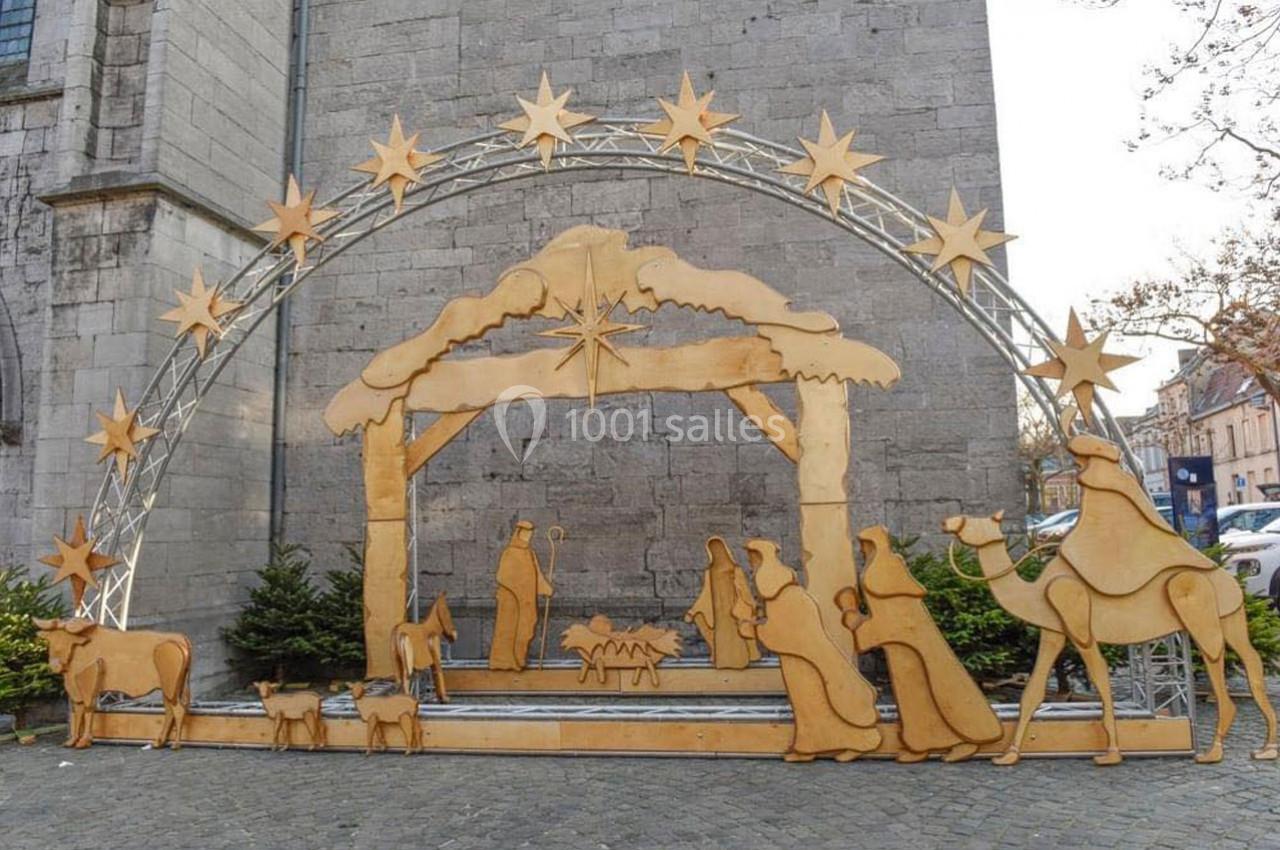 Crèche de Noël en bois avec personnages et animaux sous une arche étoilée, installée devant un mur en pierre.