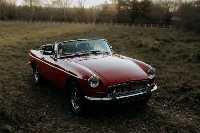 Voiture ancienne décapotable rouge garée sur une pelouse, entourée d'arbres en arrière-plan.