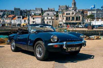 Miniature Voitures Passion #3 Roue avant d'une voiture vintage beige avec un enjoliveur chromé, stationnée sur un sol gravillonné.