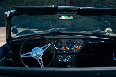 Miniature Voitures Passion #5 Roue avant d'une voiture vintage beige avec un enjoliveur chromé, stationnée sur un sol gravillonné.