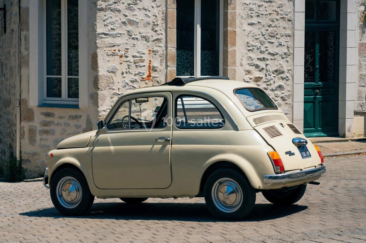 Voiture ancienne beige stationnée devant une façade en pierre avec des fenêtres et une porte verte.