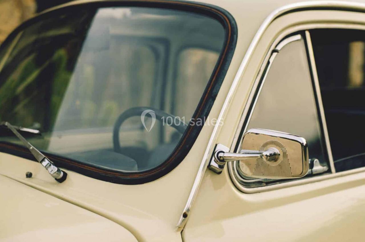 Vue rapprochée d'une voiture ancienne beige, montrant une partie de la carrosserie, le rétroviseur et l'intérieur.