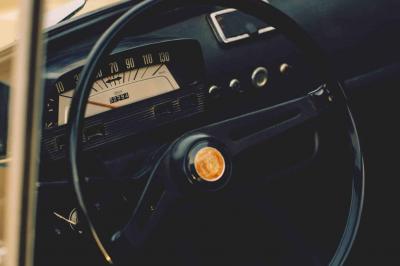 Miniature Voitures Passion #9 Roue avant d'une voiture vintage beige avec un enjoliveur chromé, stationnée sur un sol gravillonné.