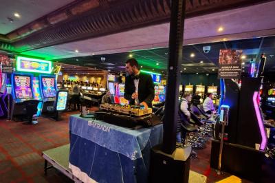Un DJ mixe sur une scène dans un casino, entouré de machines à sous et d'éclairages colorés.