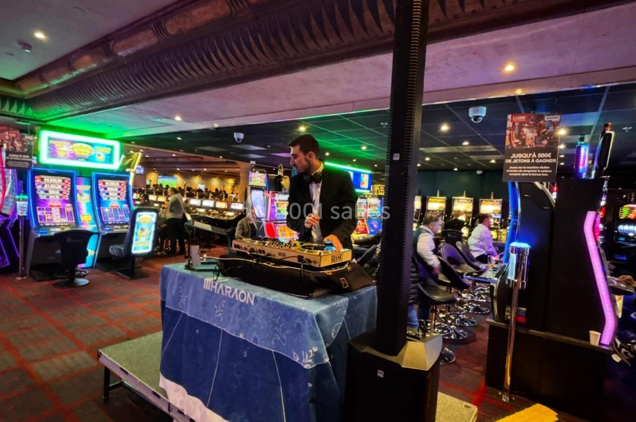 Un DJ mixe sur une scène dans un casino, entouré de machines à sous et d'éclairages colorés.