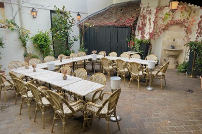 Salle à manger chaleureuse avec poutres apparentes, tables dressées, chaises rouges et cheminée en pierre.