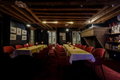 Salle à manger chaleureuse avec poutres apparentes, tables dressées, chaises rouges et cheminée en pierre.