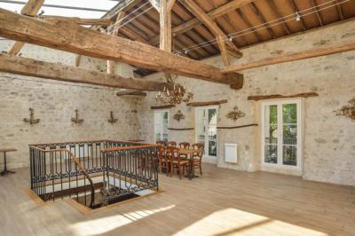 Salle à manger chaleureuse avec poutres apparentes, tables dressées, chaises rouges et cheminée en pierre.