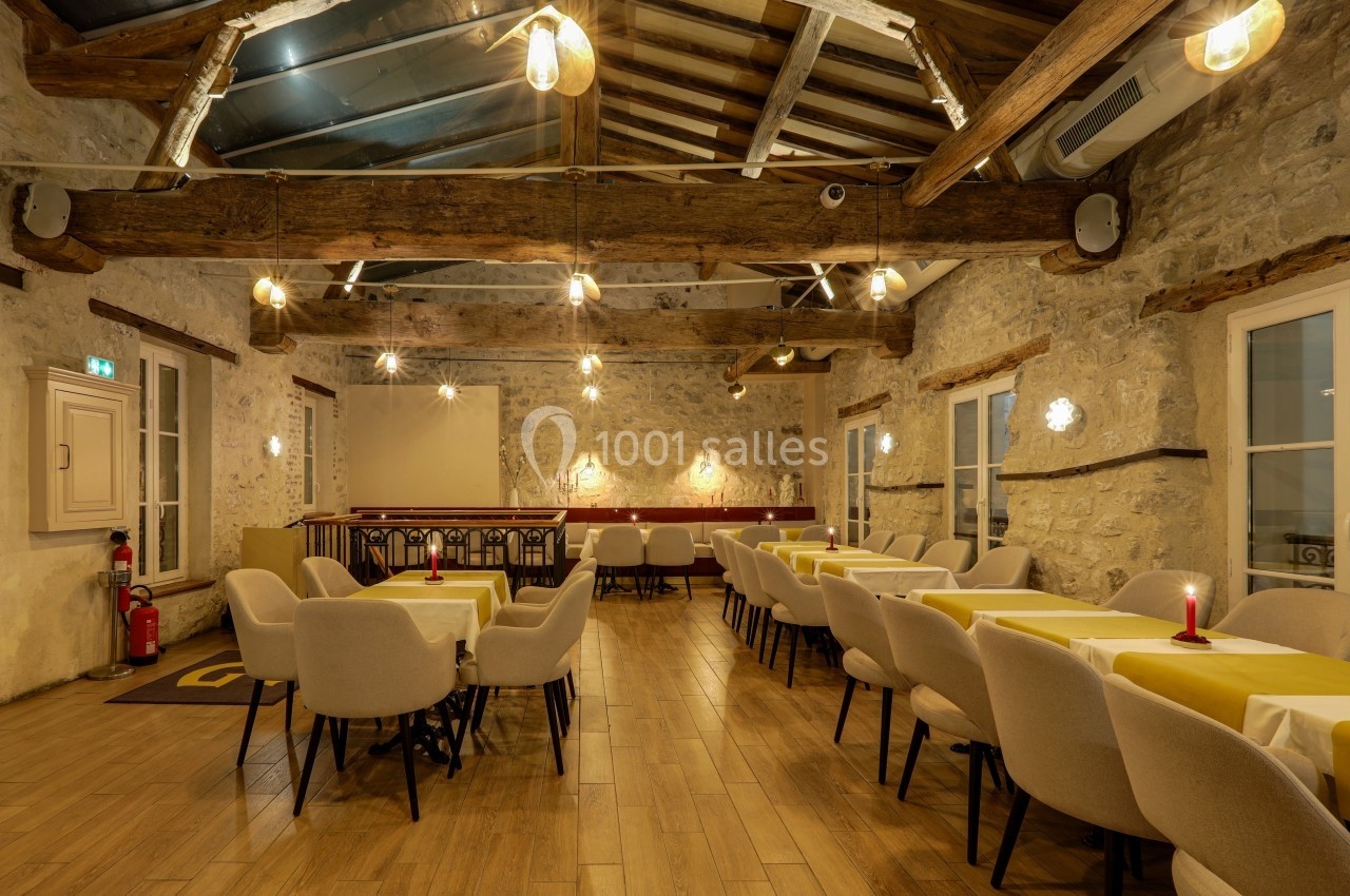 Salle de restaurant chaleureuse avec murs en pierre, poutres apparentes, tables dressées et éclairage tamisé.