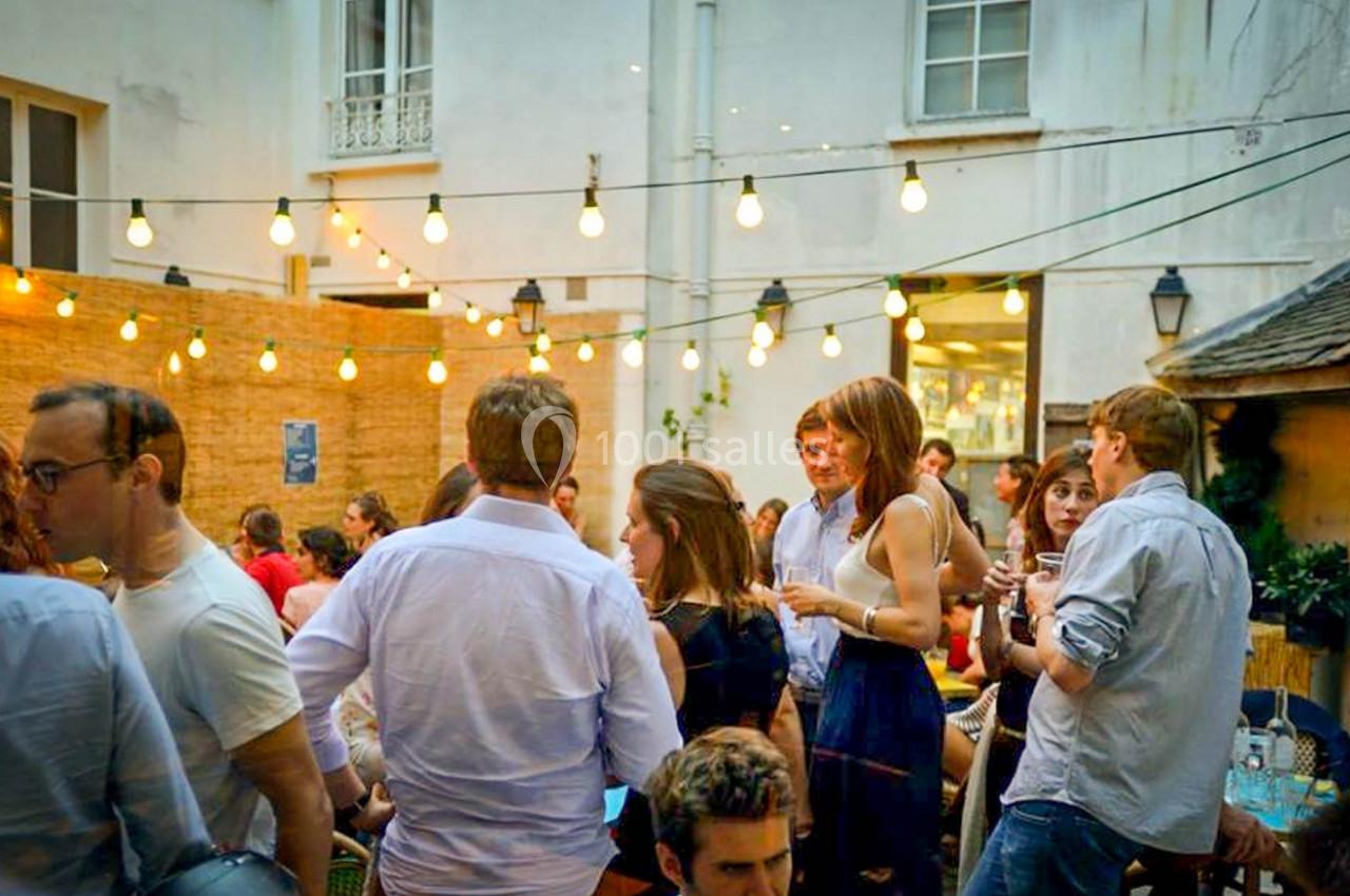 Groupe de personnes discutant dans une cour extérieure éclairée par des guirlandes lumineuses.