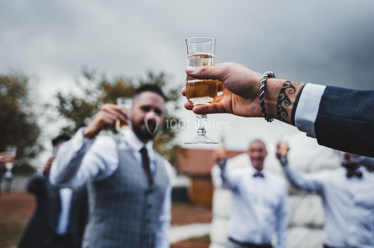 Un groupe de personnes en tenue habillée trinque avec des verres de champagne en extérieur sous un ciel nuageux.