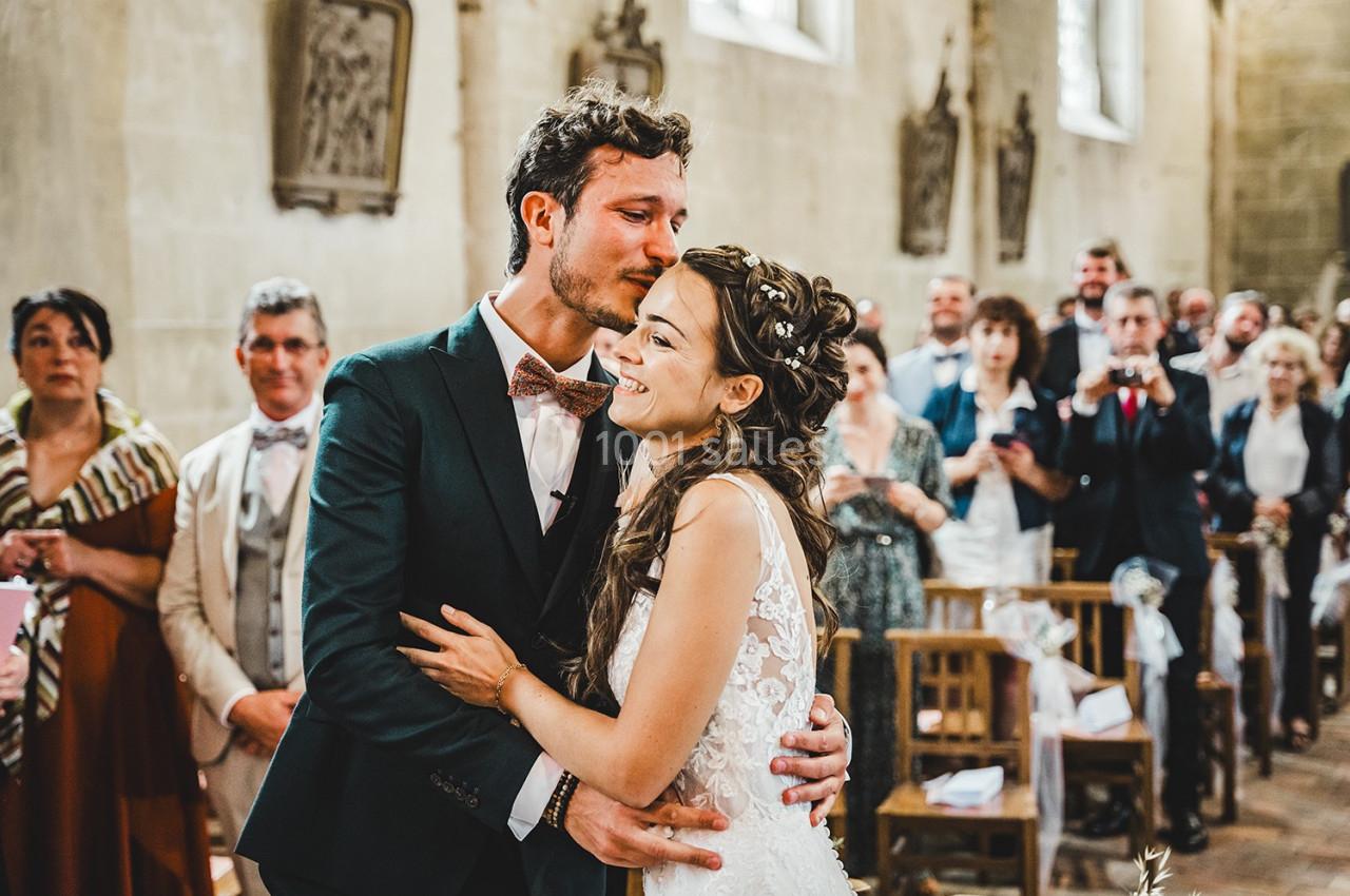 Un couple souriant s'enlace dans une église, entouré d'invités attentifs lors d'une cérémonie.